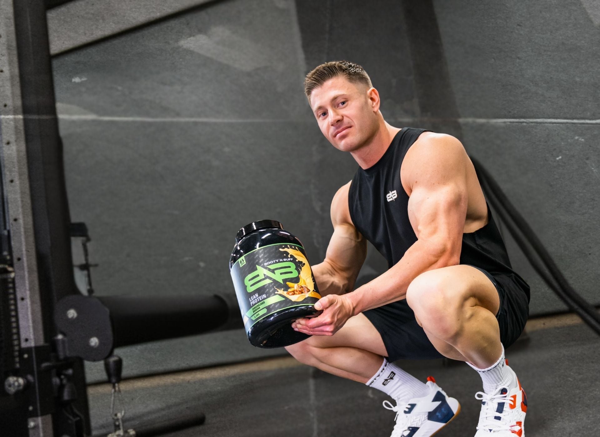 Muscular man holding a booty n buff supplement container in a gym setting